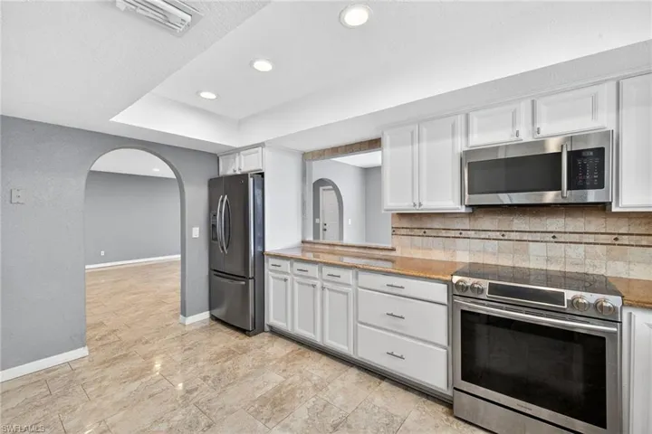 Kitchen with stainless steel appliances, white cabinetry, light stone countertops, recessed lighting, and decorative backsplash