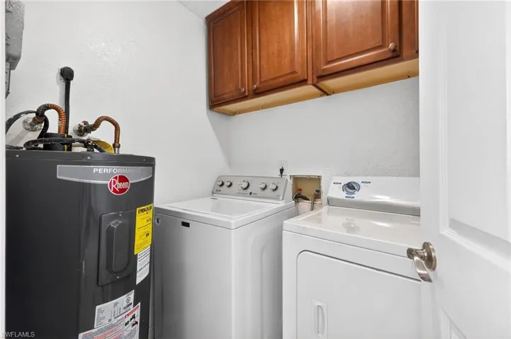 Washroom featuring electric water heater, cabinet space, and independent washer and dryer