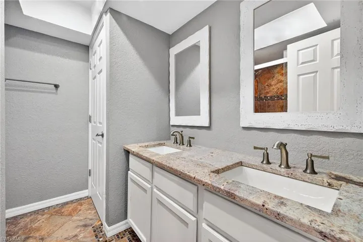 Full bathroom with a textured wall, double vanity, and stone tile floors