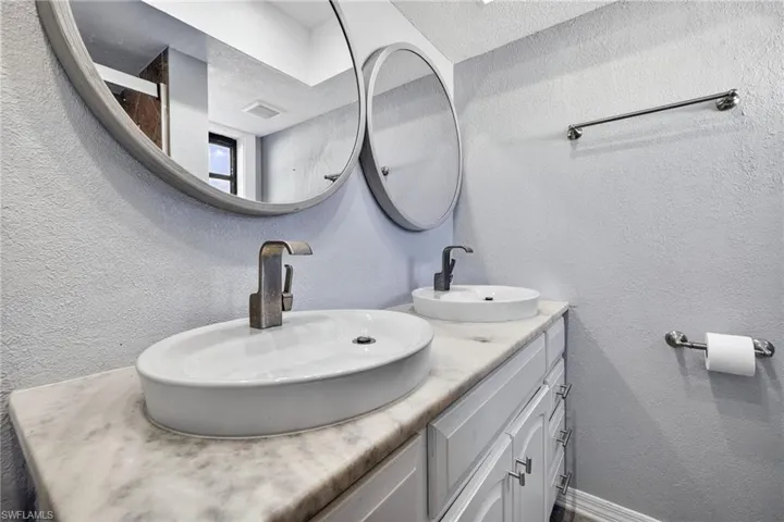 Full bathroom with a textured wall, double vanity, and a textured ceiling