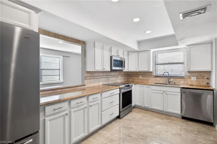 Kitchen with appliances with stainless steel finishes, white cabinets, light stone counters, tasteful backsplash, and recessed lighting