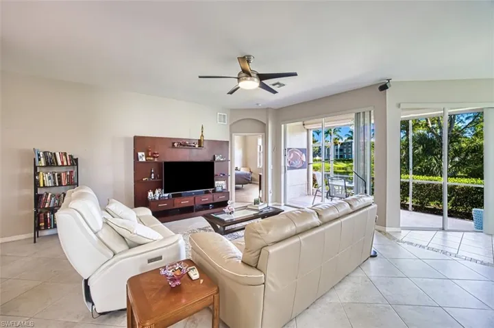 Living room with light tile patterned floors, ceiling fan, and arched walkways