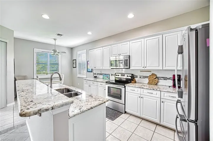 Kitchen featuring white cabinets, stainless steel appliances, a kitchen island with sink, light stone counters, and a ceiling fan