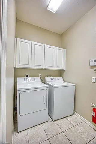 Laundry room with a textured wall, cabinet space, washing machine and dryer, a textured ceiling, and light tile patterned floors