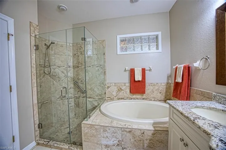Full bath with a stall shower, a bath, vanity, and a textured wall