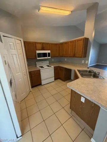 Kitchen featuring wood finish cabinets, white appliances, light countertops, lofted ceiling, and light tile patterned flooring