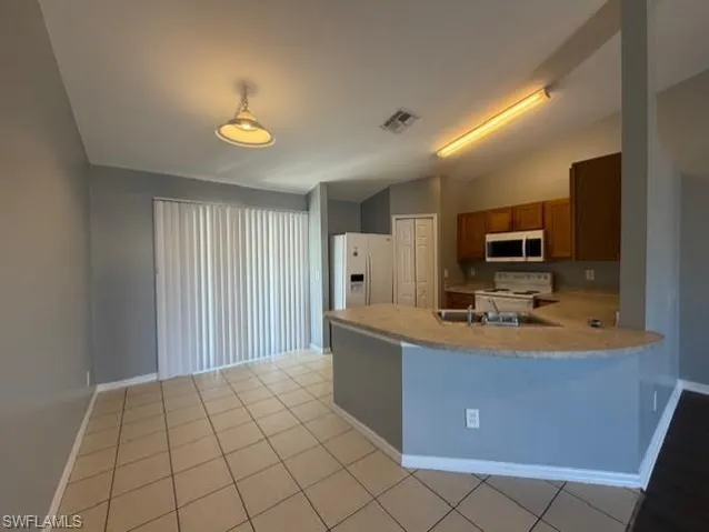Kitchen with vaulted ceiling, light countertops, wood finish cabinets, white appliances, and a peninsula