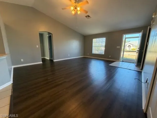 Empty room with arched walkways, vaulted ceiling, dark wood finished floors, and a ceiling fan
