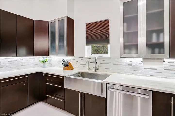 Kitchen featuring dark brown cabinets, stainless steel dishwasher, and glass insert cabinets