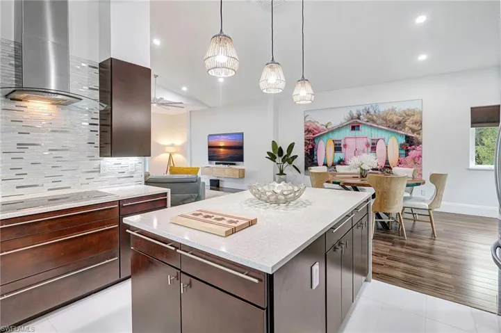Kitchen with wall chimney exhaust hood, dark brown cabinets, a kitchen island, hanging light fixtures, and backsplash