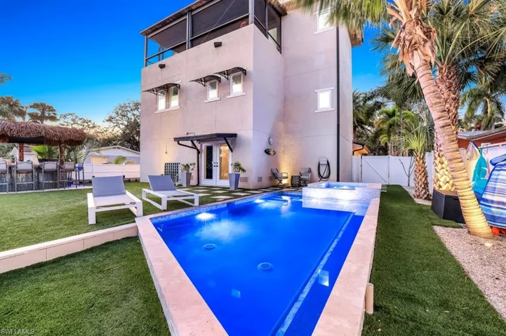 Back of house featuring a fenced backyard, a patio area, a pool with connected hot tub, stucco siding, and a third-story lanai