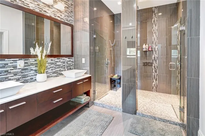 Full bathroom with double vanity, a shower stall, tile walls, and backsplash
