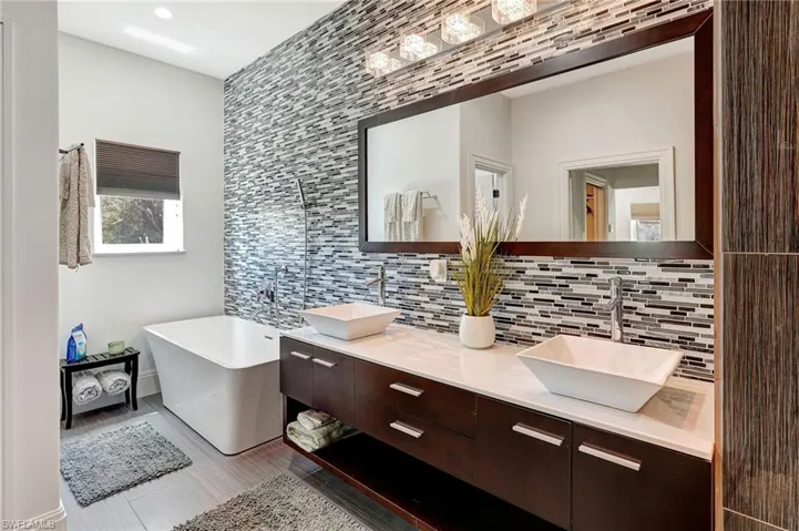 Full bath with a freestanding tub, double vanity, backsplash, and dark wood-style flooring
