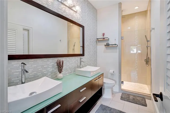 Bathroom featuring a frameless shower, tile walls, decorative backsplash, light tile patterned floors, and double vanity