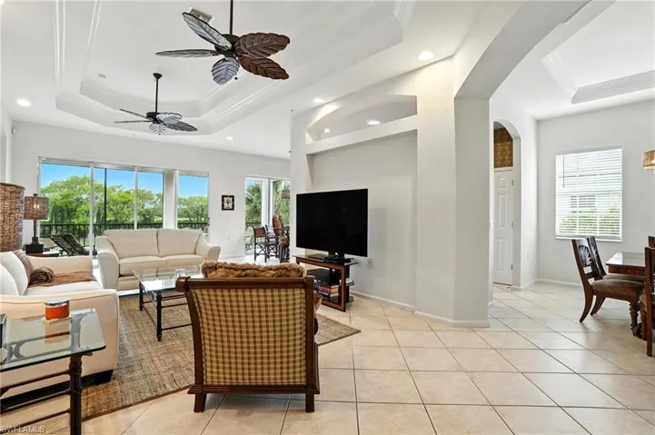 Living area featuring a raised ceiling, crown molding, light tile patterned flooring, a ceiling fan, and recessed lighting