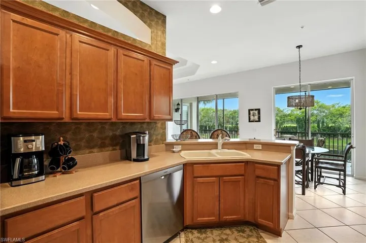 Kitchen featuring a peninsula, backsplash, brown cabinetry, dishwasher, and hanging light fixtures