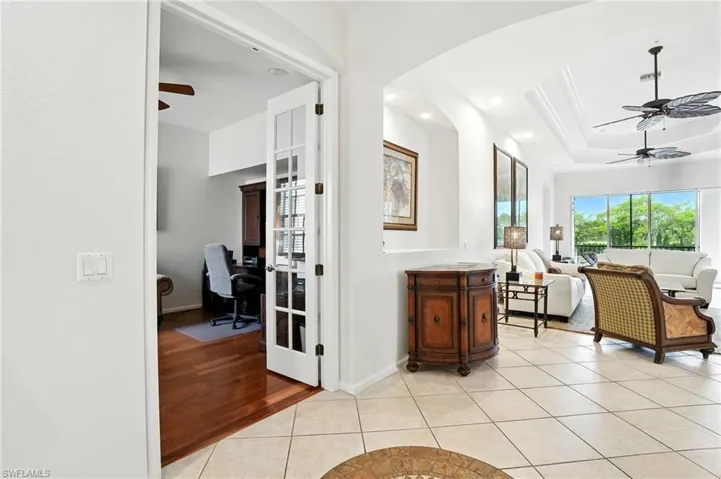 Corridor with light tile patterned flooring, an office area, a raised ceiling, recessed lighting, and arched walkways
