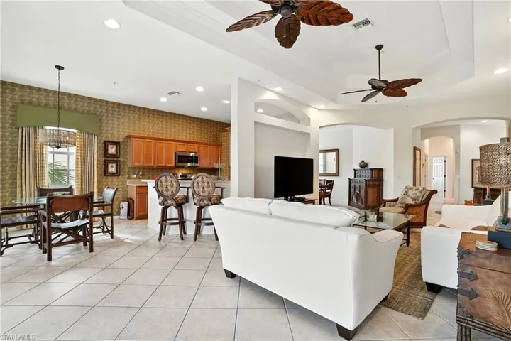 Living area with a chandelier, recessed lighting, light tile patterned flooring, a tray ceiling, and arched walkways