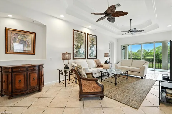 Living area featuring crown molding, a raised ceiling, light tile patterned floors, arched walkways, and ceiling fan