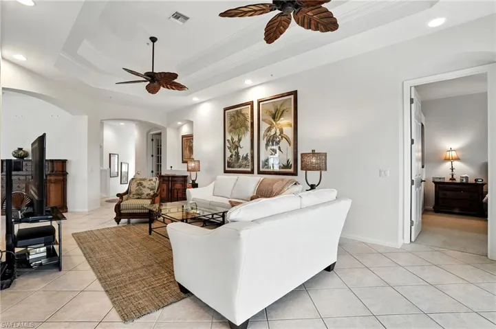Living area featuring a tray ceiling, arched walkways, light tile patterned floors, recessed lighting, and crown molding
