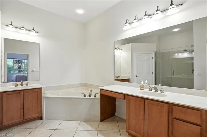 Bathroom featuring a stall shower, light tile patterned floors, a garden tub, two vanities, and ensuite bathroom