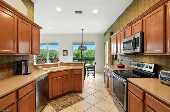 Kitchen featuring backsplash, stainless steel appliances, brown cabinetry, a peninsula, and recessed lighting