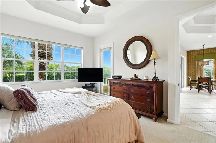 Bedroom with a tray ceiling, ornamental molding, light carpet, a ceiling fan, and light tile patterned flooring