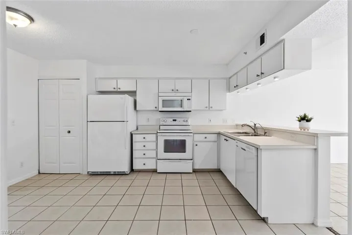 Kitchen featuring white appliances, white cabinets, sink, a textured ceiling, and light tile patterned flooring