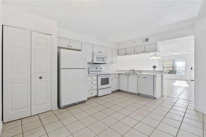 Kitchen with sink, white cabinets, light tile patterned flooring, and white appliances