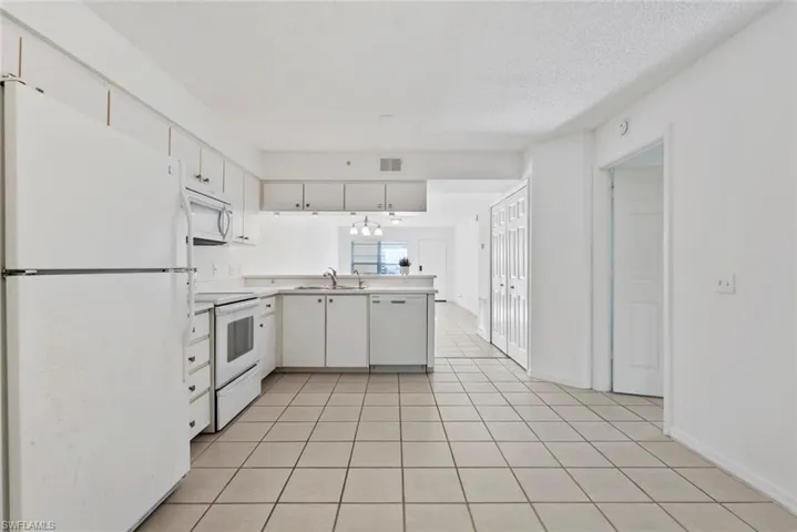 Kitchen featuring kitchen peninsula, white appliances, sink, white cabinetry, and light tile patterned flooring
