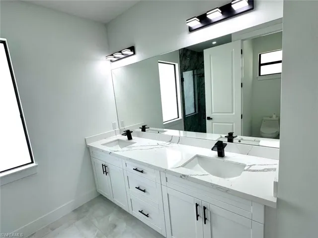 Bathroom featuring marble finish flooring, double vanity, toilet, baseboards, and a shower