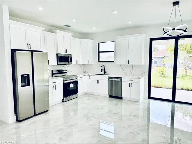 Kitchen featuring appliances with stainless steel finishes, a sink, tasteful backsplash, light marble finish floors, and recessed lighting