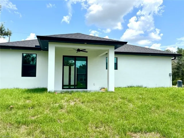 Rear view of property with stucco siding, a yard, a shingled roof, and a ceiling fan