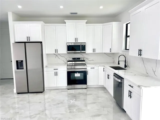Kitchen featuring appliances with stainless steel finishes, a sink, recessed lighting, light marble finish flooring, and decorative backsplash