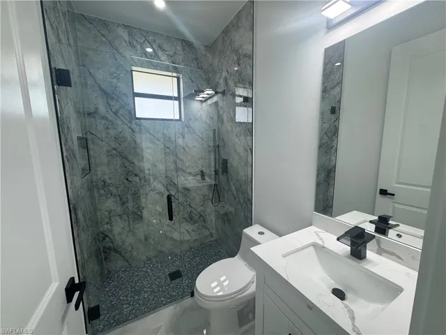 Full bathroom with a marble finish shower, toilet, marble finish floors, and vanity
