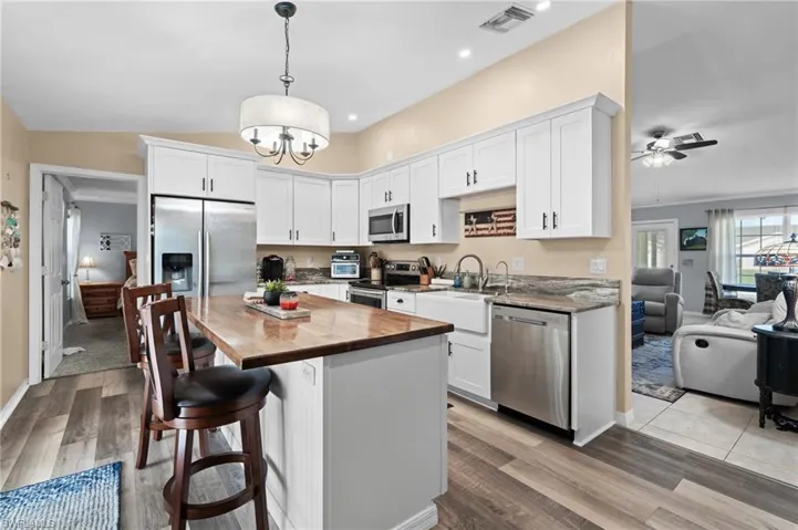 Kitchen featuring stainless steel appliances, light wood-type flooring, hanging light fixtures, and white cabinets