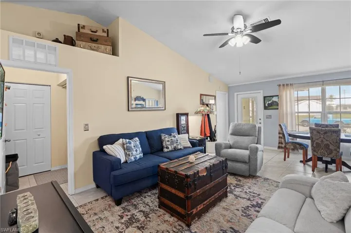 Living room featuring light tile patterned flooring, ceiling fan, and vaulted ceiling