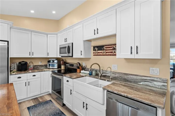Kitchen with white cabinetry, appliances with stainless steel finishes, light hardwood / wood-style flooring, and dark stone countertops