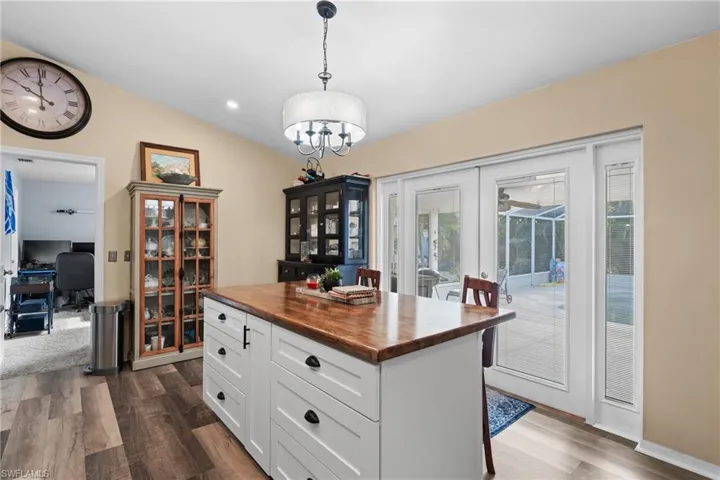 Kitchen featuring lofted ceiling, butcher block counters, white cabinetry, decorative light fixtures, and a kitchen island