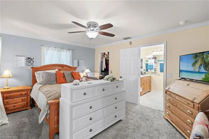 Bedroom featuring crown molding, connected bathroom, a spacious closet, and light colored carpet