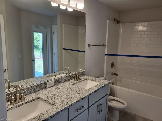 Full bathroom with double vanity, shower / bath combination, and a textured wall