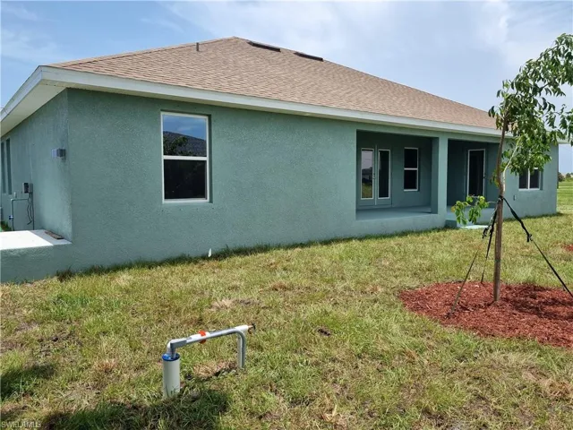 Rear view of property featuring stucco siding, a yard, and roof with shingles