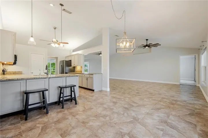 Kitchen featuring stainless steel refrigerator, light tile patterned floors, white cabinets, ceiling fan with notable chandelier, and a kitchen breakfast bar