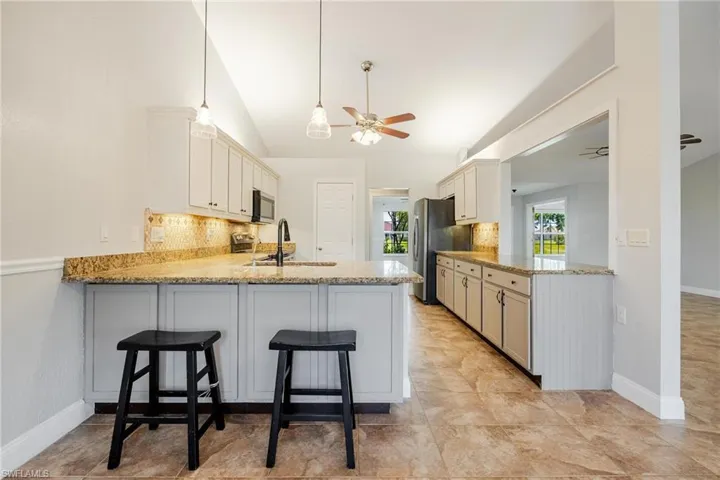 Kitchen with kitchen peninsula, light stone counters, ceiling fan, decorative backsplash, and sink
