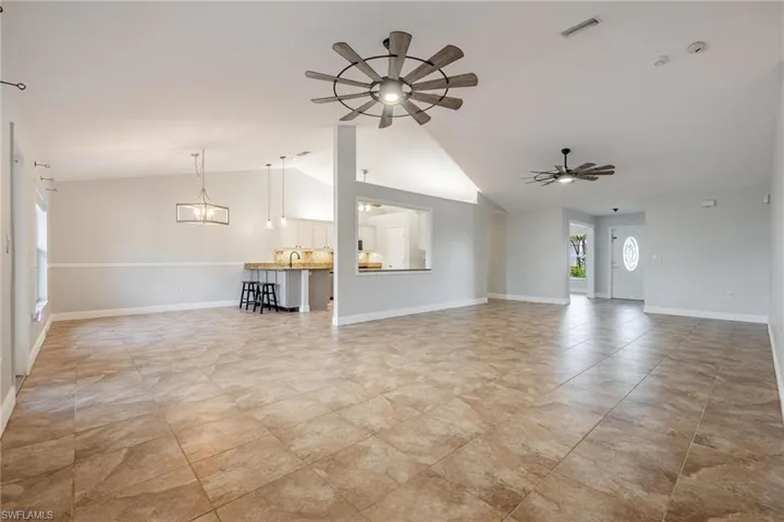 Unfurnished living room featuring sink, ceiling fan with notable chandelier, vaulted ceiling, and light tile patterned floors