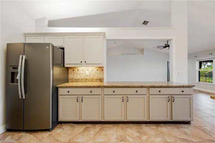 Kitchen with light tile patterned flooring, cream cabinetry, stainless steel fridge with ice dispenser, light stone countertops, and lofted ceiling
