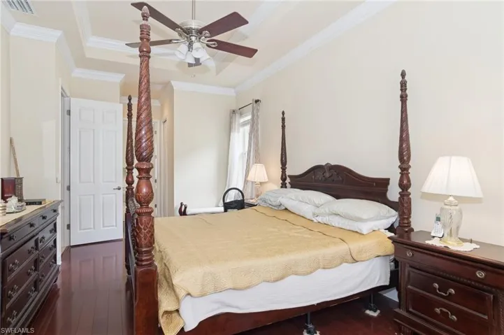 Bedroom with dark wood-type flooring, ornamental molding, a tray ceiling, and a ceiling fan