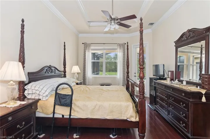 Bedroom with dark wood-type flooring, crown molding, a tray ceiling, and a ceiling fan