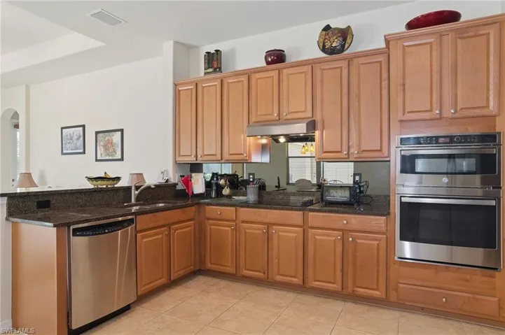 Kitchen featuring stainless steel appliances, under cabinet range hood, dark stone countertops, and arched walkways