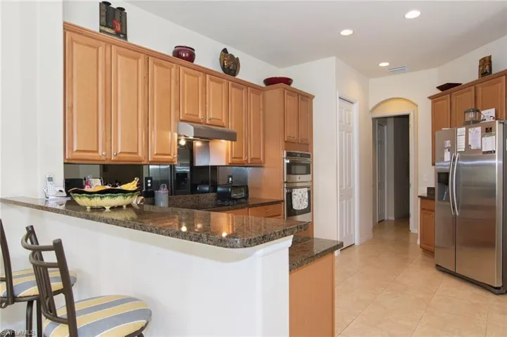 Kitchen featuring appliances with stainless steel finishes, under cabinet range hood, a peninsula, a kitchen bar, and dark stone counters